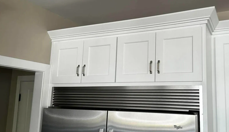 Finished white shaker cabinets with crown molding built in above a stainless steel refrigerator