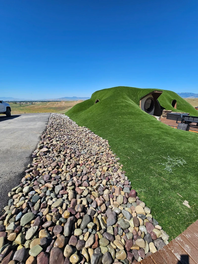 Finished decorative river rock bed running along the driveway beside the green turf-covered hillside home